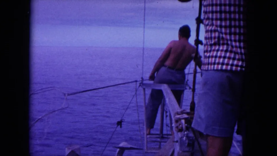 1964 Hawaii 8mm frame showing the stern area, a man leaning near fishing lines, and another adult partly blocking the right side.