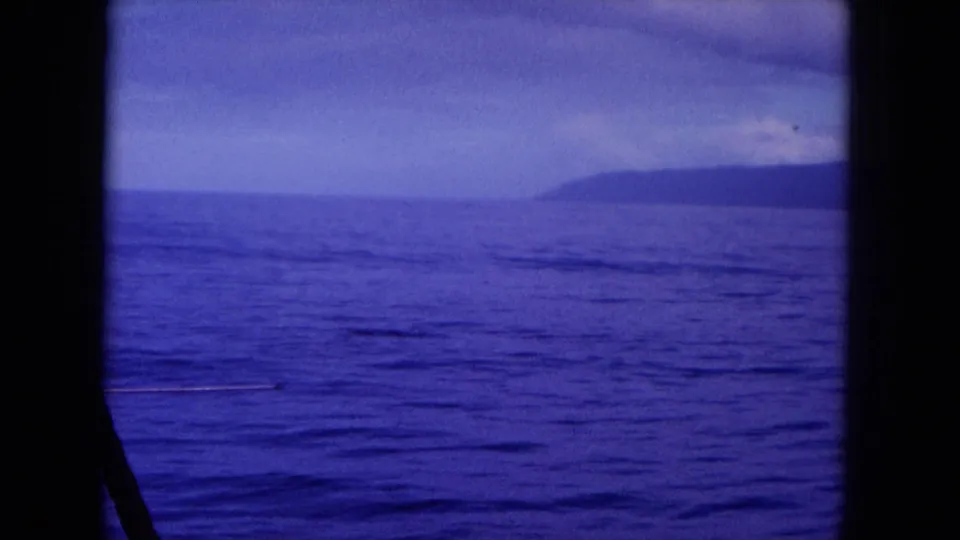 1964 Hawaii home-movie frame showing calm ocean water and a distant shoreline, with no people visible in this still.