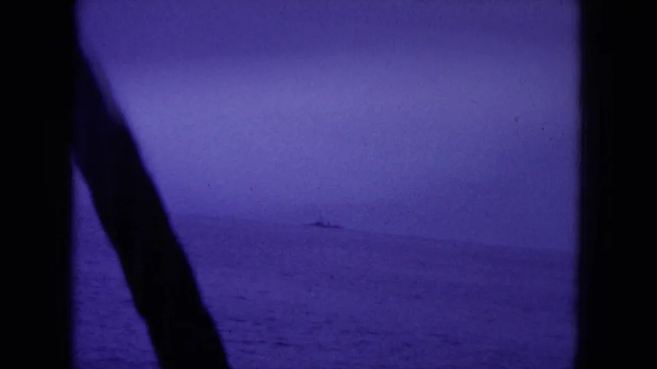 1964 Hawaii home-movie frame showing open water through dark boat structure, with a small vessel faintly visible on the horizon.