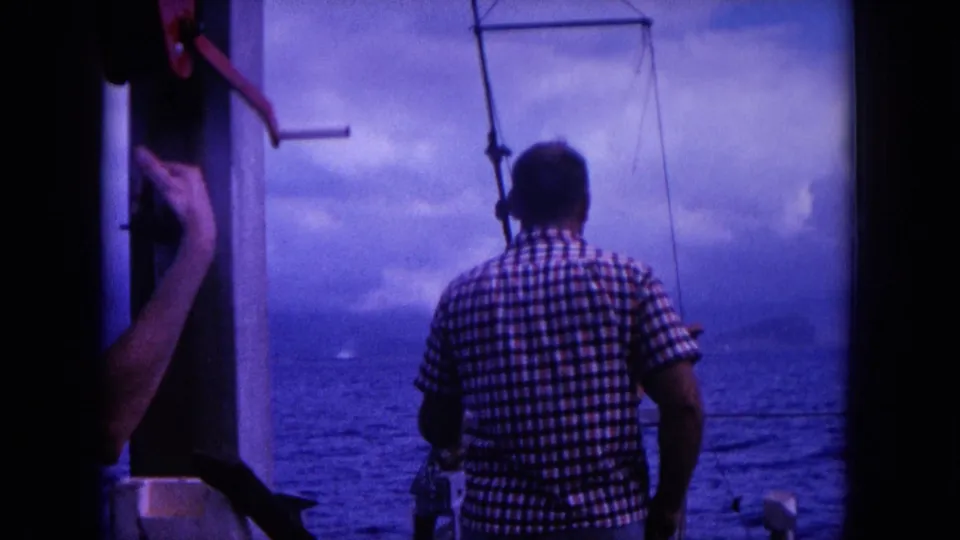1964 Hawaii 8mm frame with a man in a checkered shirt looking out over the ocean from a boat with rigging visible.