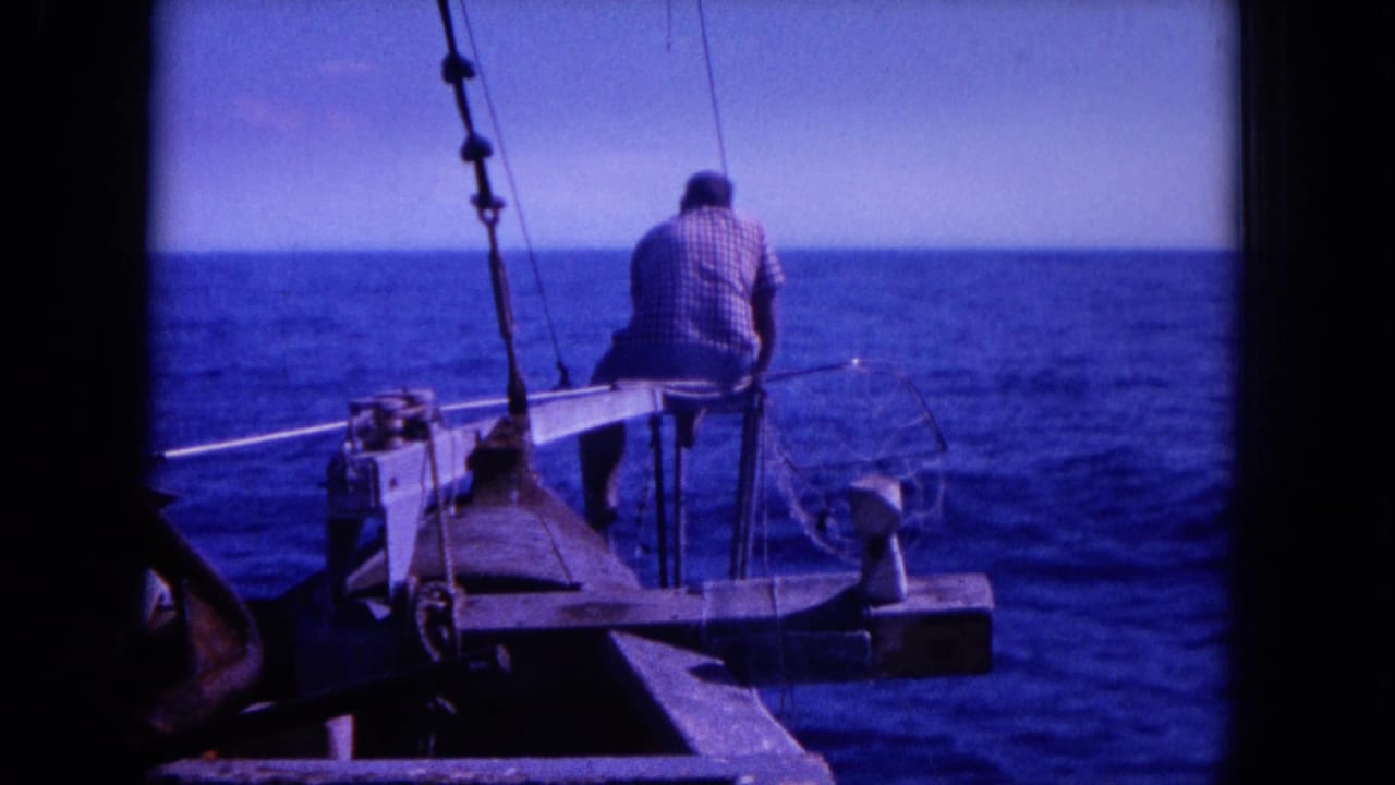 Man seated on a small boat edge facing the open ocean.