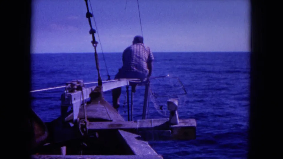 1964 8mm Hawaii boating frame with a seated man, deck hardware, vertical rigging, and open sea under a pale sky.