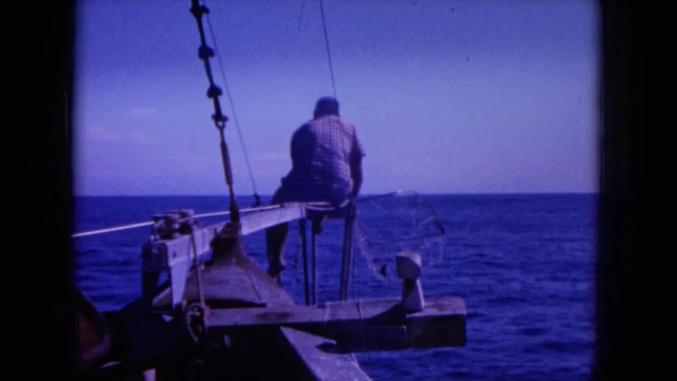 Vintage 8mm frame from Hawaii showing a man seated on a small boat with possible fishing gear and a wide ocean horizon.