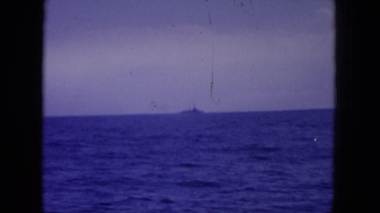 Distant ship on the horizon viewed across blue ocean through dark window framing.