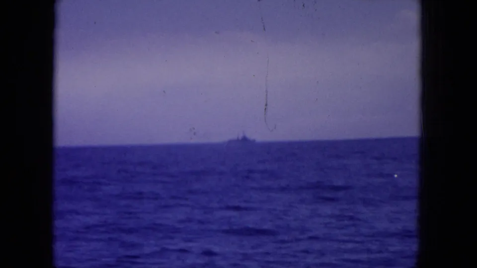 1964 Hawaii-area 8mm frame showing a small distant ship on the horizon beyond blue ocean, seen through a dark vessel window.