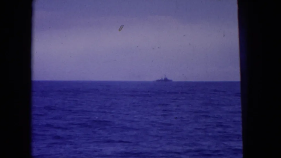 1964 Hawaii-area 8mm frame with a small ship silhouette on the horizon, blue ocean foreground, and visible film wear.