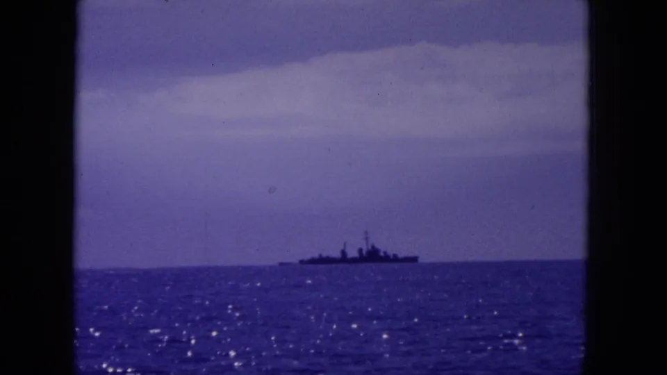 1964 Hawaii home-movie frame with a distant warship-like vessel crossing the horizon under a purple-tinged sky.