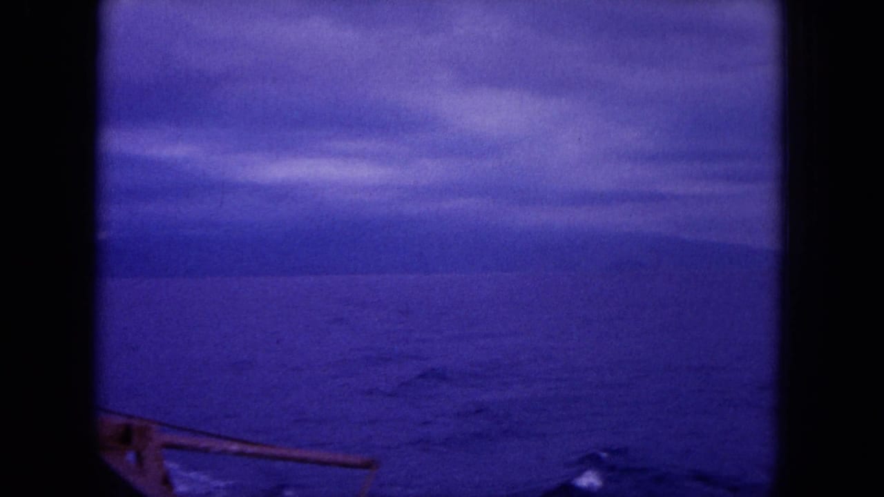 Blue-tinted ocean view through dark film borders with a faint coastline and boat hardware at lower left.