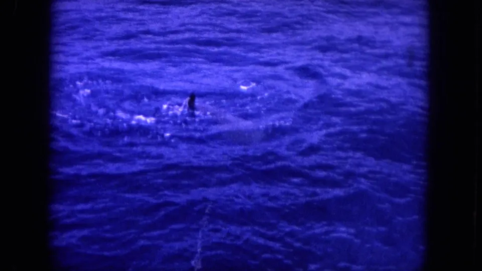 1964 Hawaii 8mm frame showing rippling blue ocean near a boat, with a small dark shape breaking the water surface.