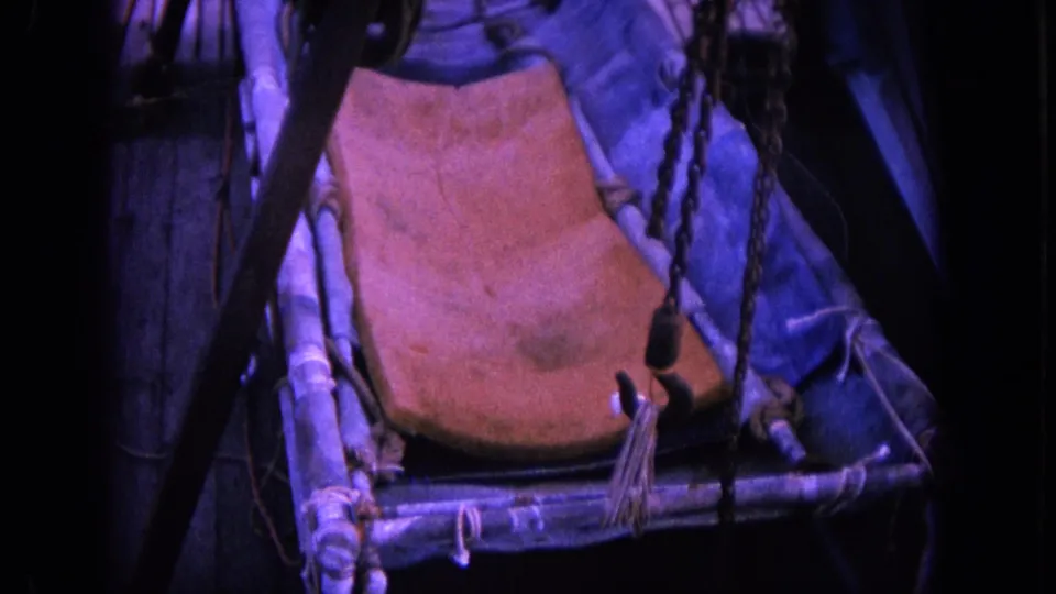 Close 1964 Hawaii 8mm view of the fishing boat deck, centered on a sling chair surrounded by ropes, chain, railings, and rigging.