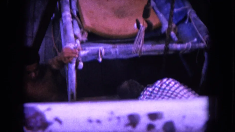1964 Hawaii 8mm frame showing deck rigging and sling chair, with part of a man in a checkered shirt visible near the lower right edge.