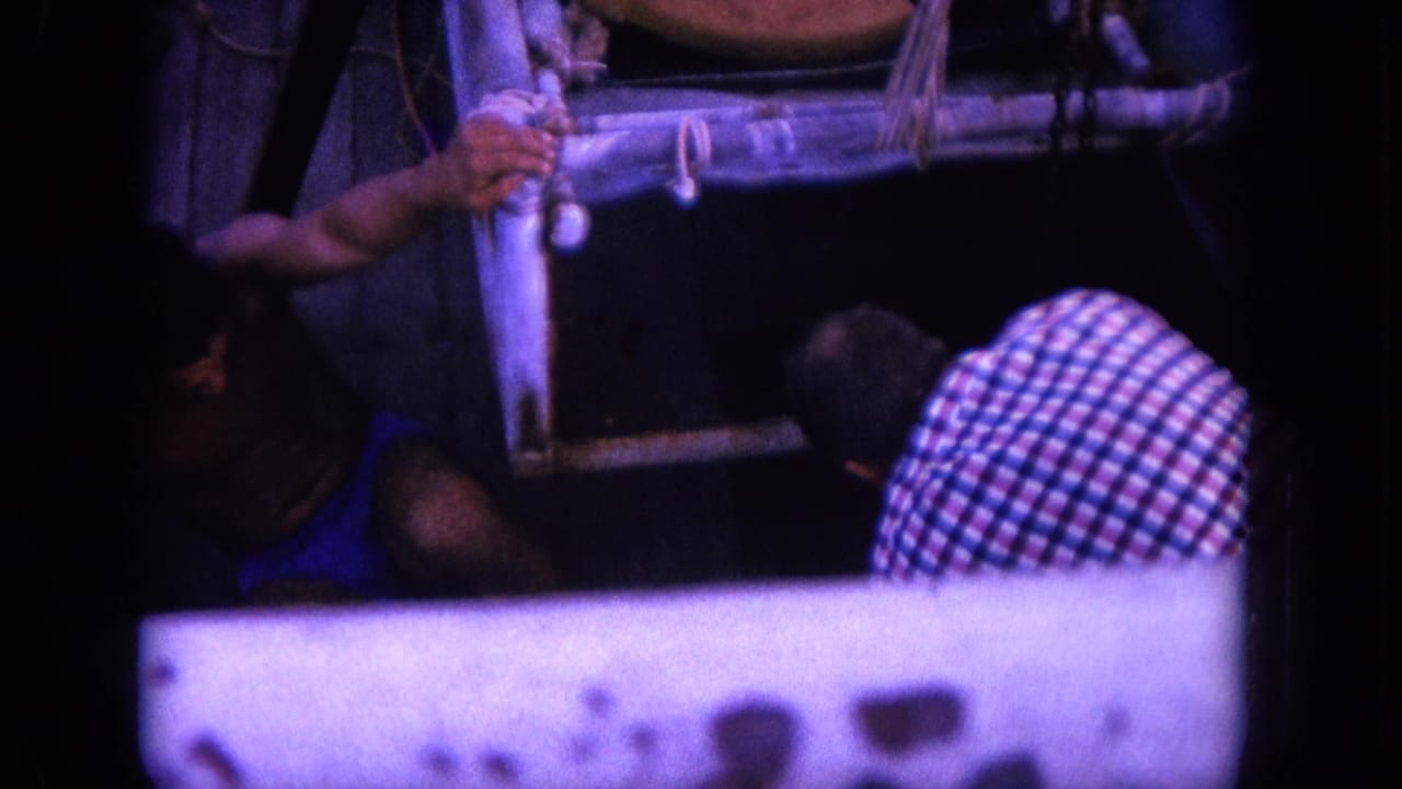 Men at a boat rail pull a tied shark near the side of a small wooden boat.