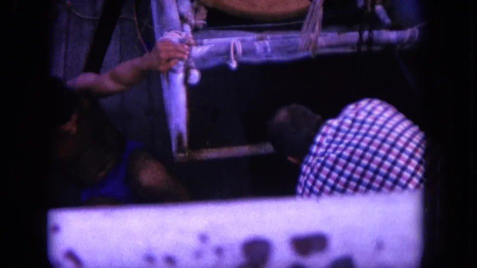 1964 Hawaii 8mm frame showing men at a small boat rail handling rope as a tied shark is brought alongside.