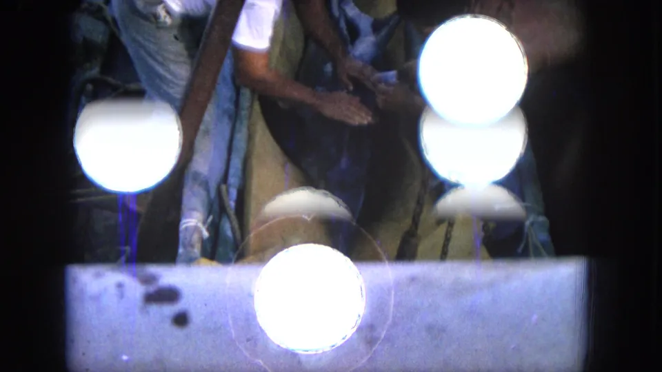 Deck-level 1964 Hawaii 8mm frame with partially visible people handling gear near the boat rail as bright circular exposure artifacts obscure part of the view.