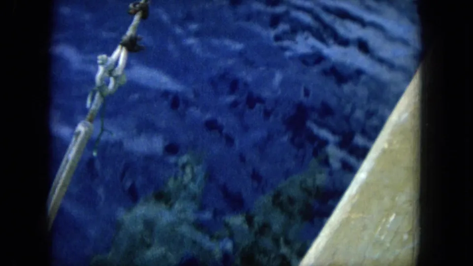 Shipboard 8mm frame from Hawaii showing a rope or line over deep blue water, with the vessel edge along the right side.