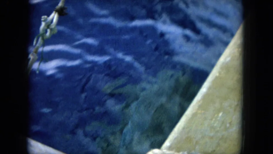 1964 Hawaii 8mm frame showing a dolphin or marine animal near the surface beside a boat edge in open water.