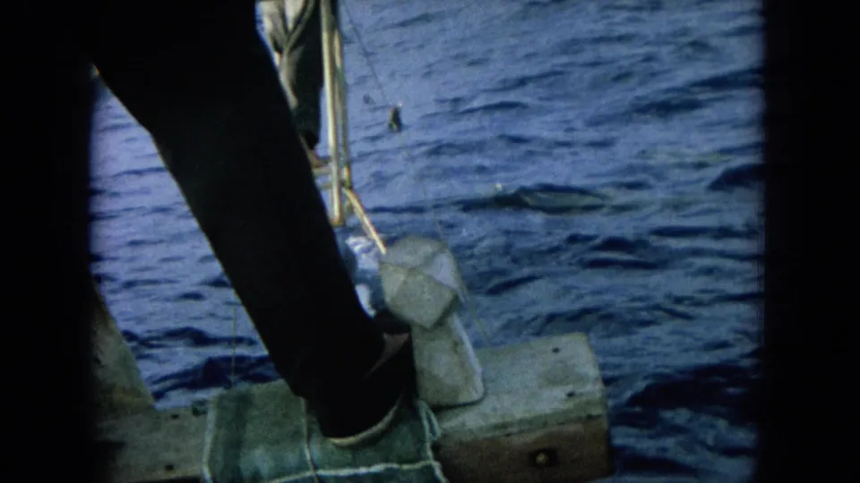 Close onboard view of a person's leg and foot near a metal boat platform, with blue ocean water filling the background.