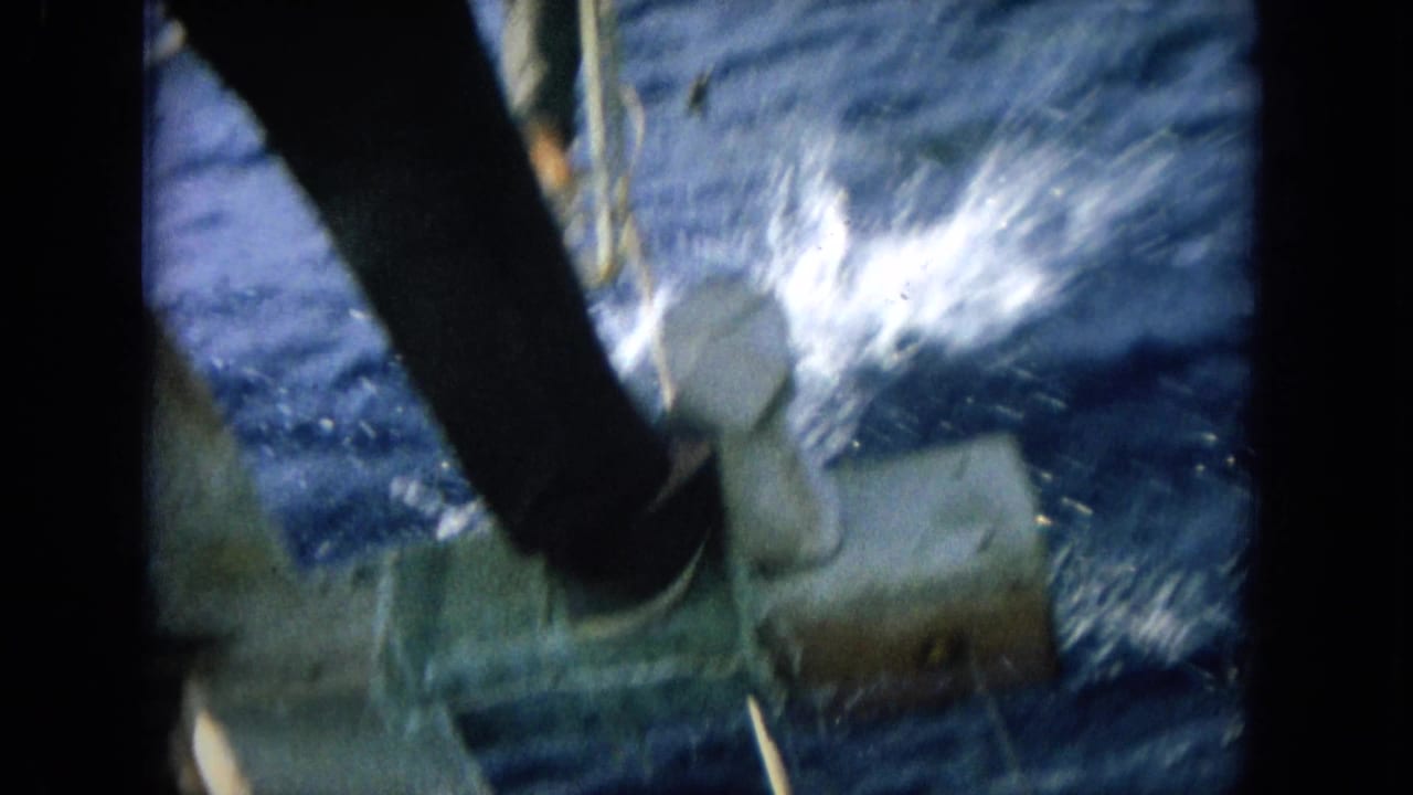 1964 Hawaii 8mm frame showing a person in dark clothing by a boat rail with sea spray and churning blue water below.