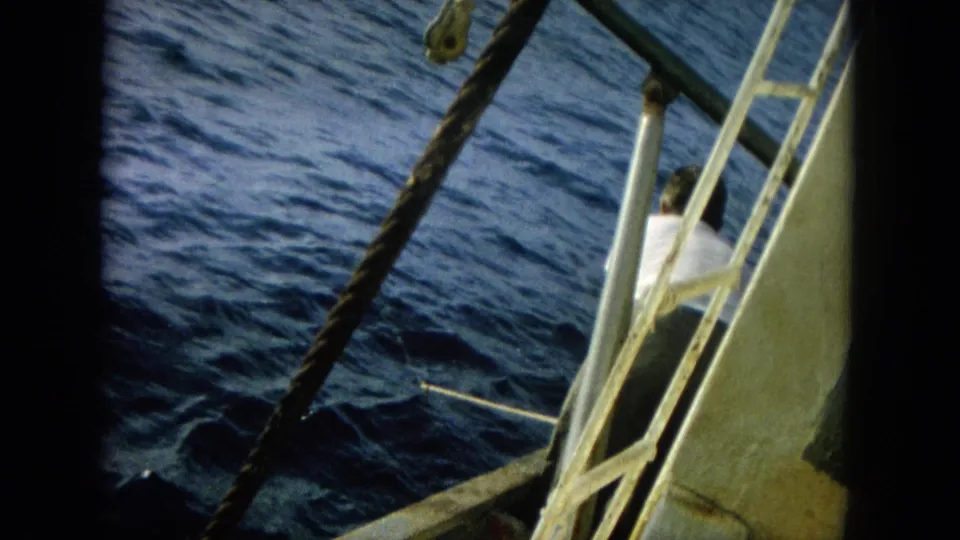 1964 Hawaii 8mm frame showing boat rigging, railings, rope, and a man in a white shirt beside the open sea.