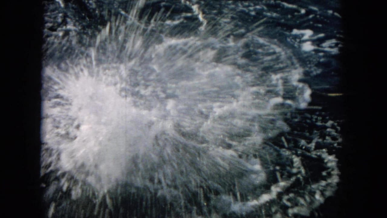 Large burst of white spray on dark ocean water within a film-frame border.