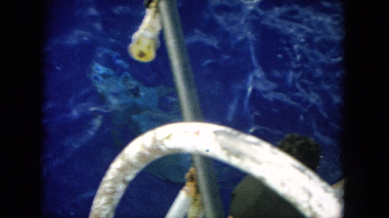 Handheld 8mm view from a boat in Hawaii, with deep blue water, curved railings, and a partially visible person near the edge.