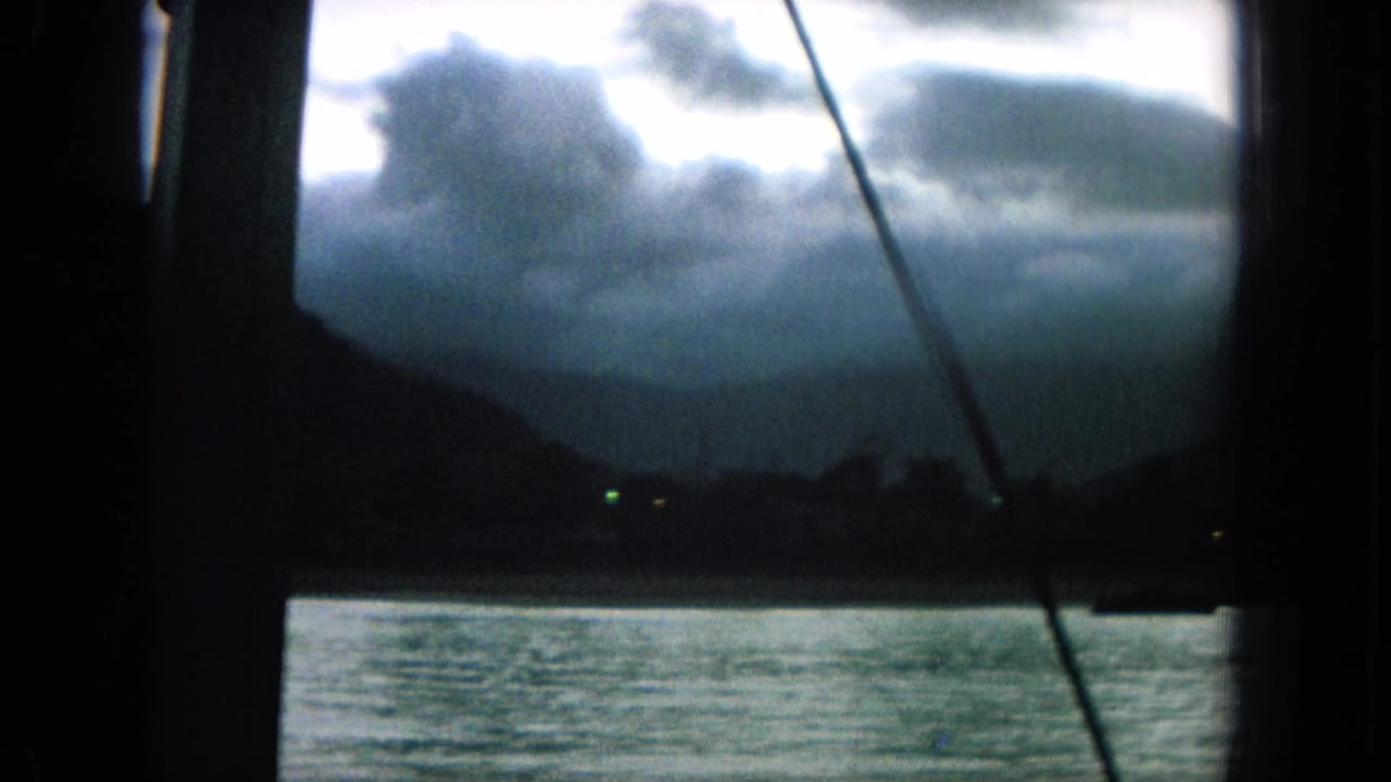 Moody water view with distant hills, clouds, rigging, and shoreline lights.