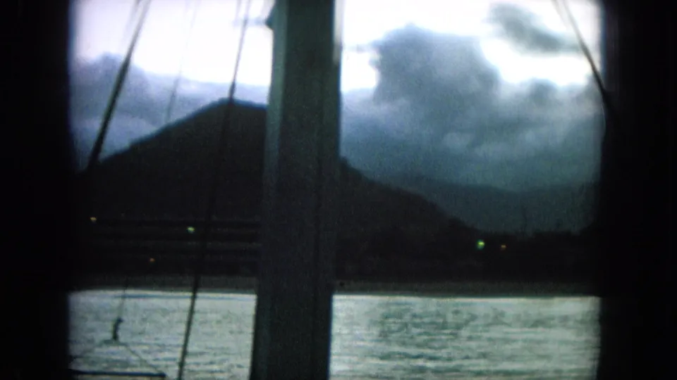 1964 8mm frame identified as Oahi, Hawaii, showing a low-light boat view of water, hills, clouds, and faint lights.
