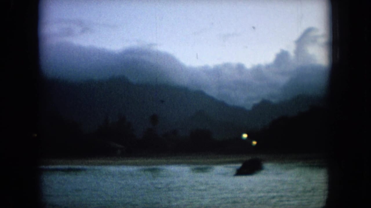 Harbor shoreline at dawn with dark mountain ridges, small lights, water, and a silhouetted post.