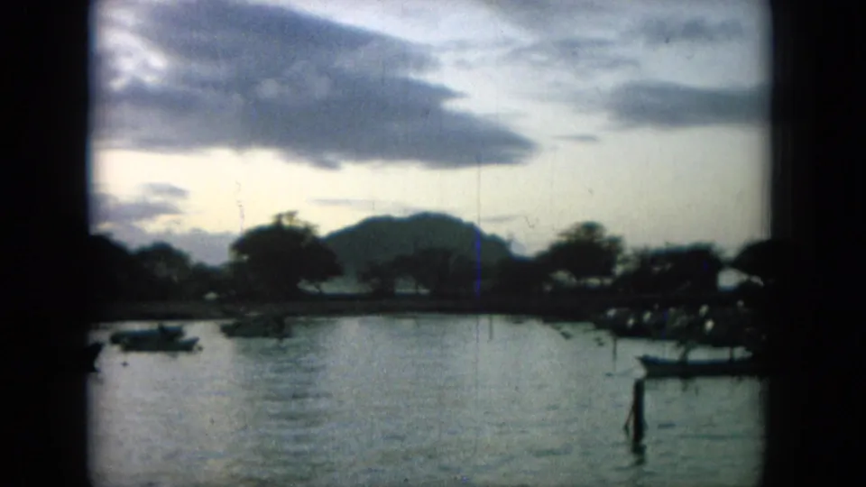 1964 Oahi, Hawaii harbor view showing small boats on calm water, trees along the shoreline, low mountains, and a bright clouded morning sky.