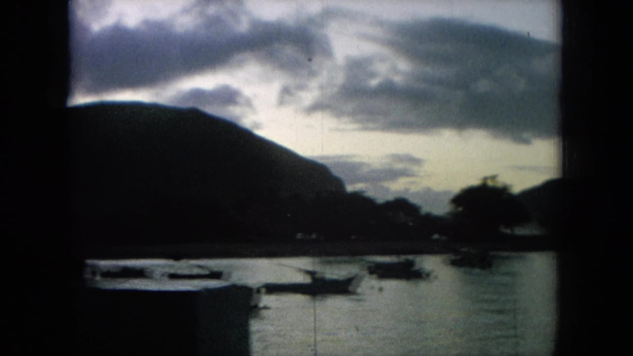 Boats on calm water with a large dark mountain and cloudy sky behind them.