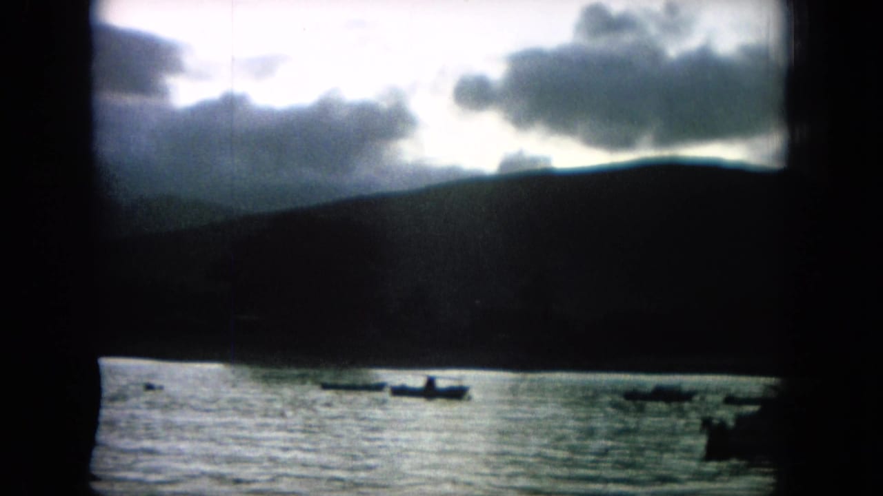 Small boats on water below dark hills and heavy clouds, seen through a dark frame.