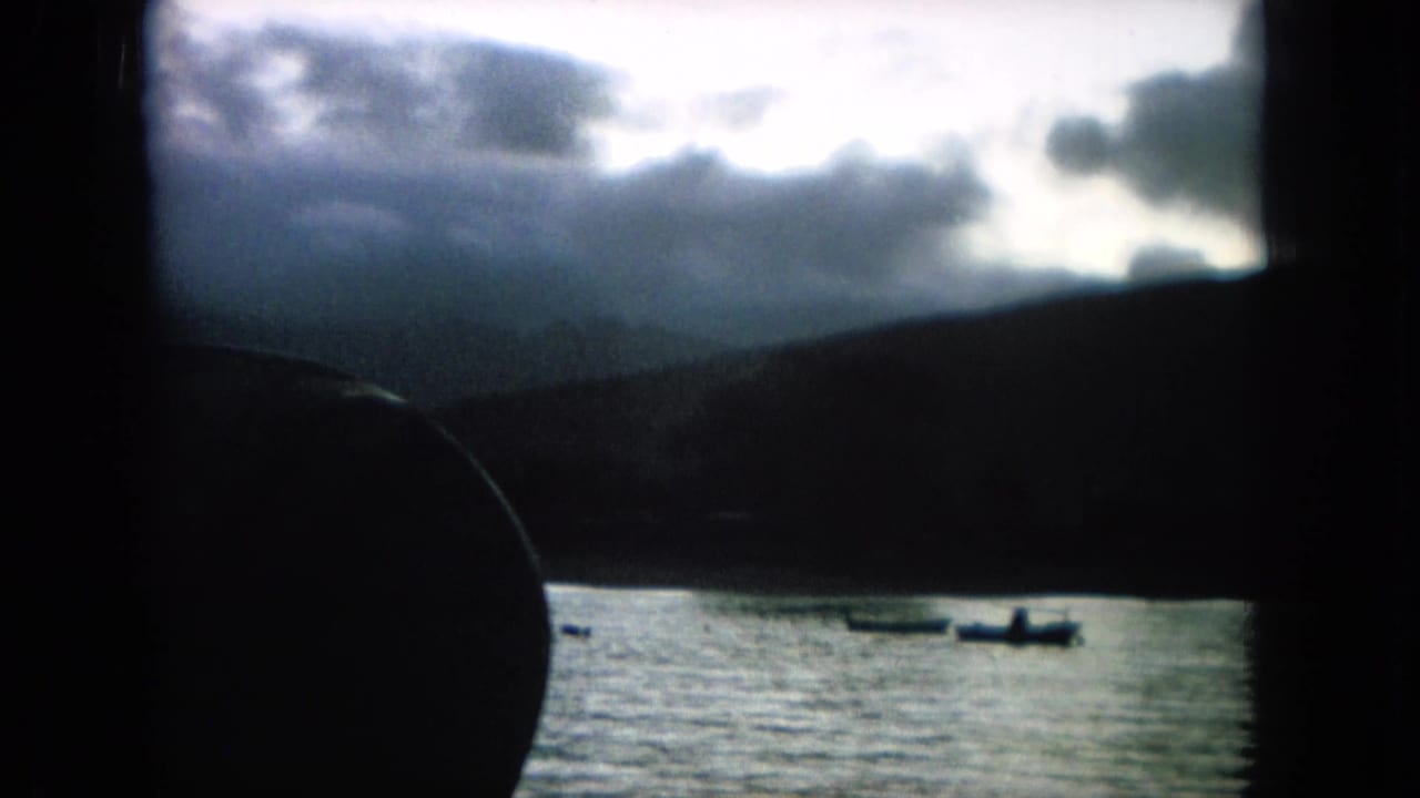 Boats on water with dark hills and clouds, partly blocked by a foreground silhouette.