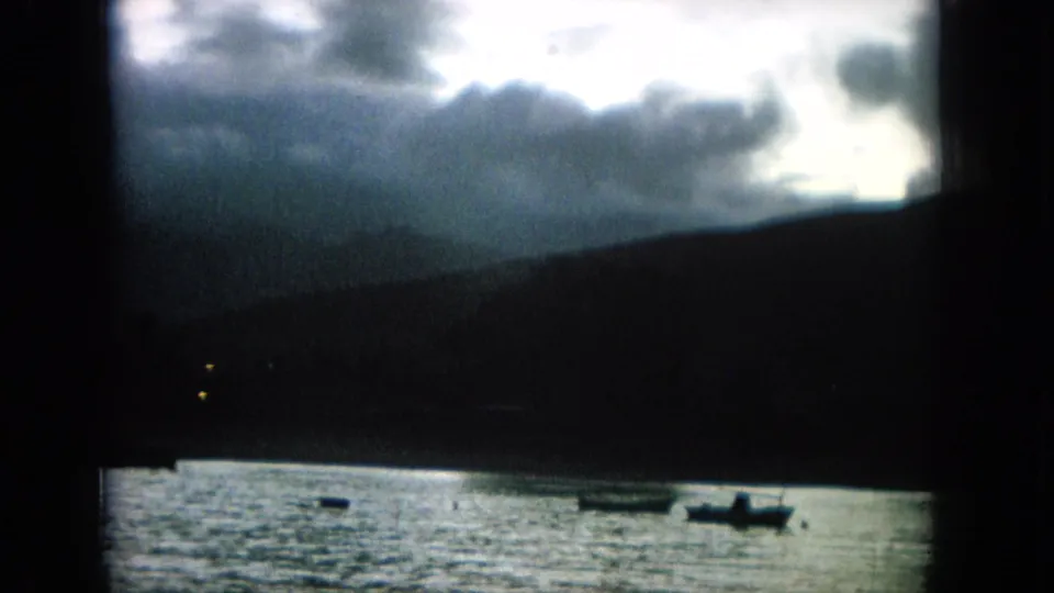 The 8mm frame shows a dim Hawaii water scene with small boats, dark hills, and dense clouds across the horizon.