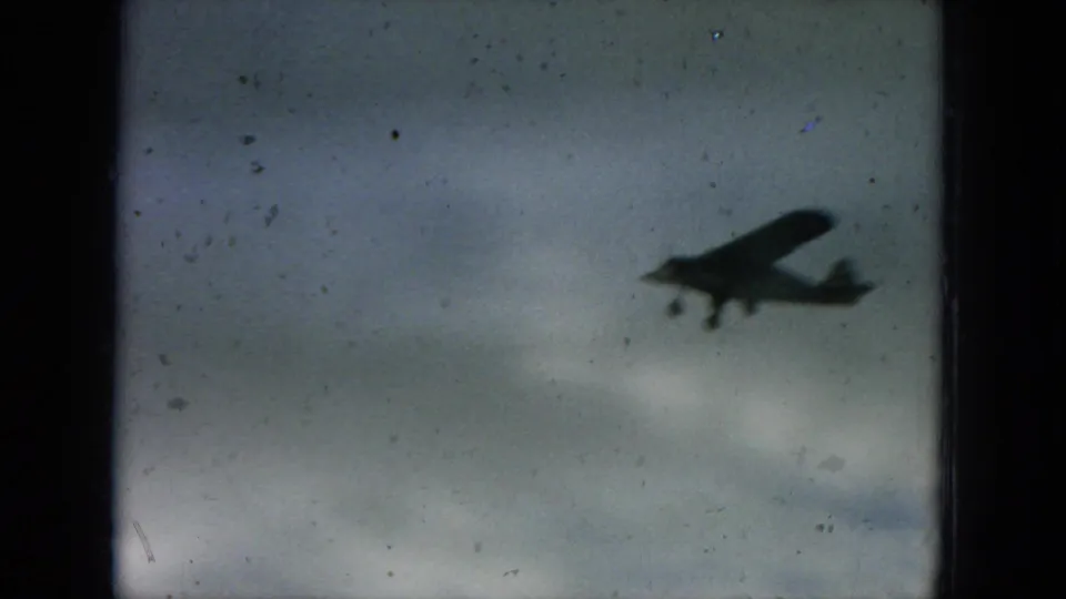 Small propeller plane appears in silhouette against a gray sky in this 1964 Hawaii 8mm home-movie frame.