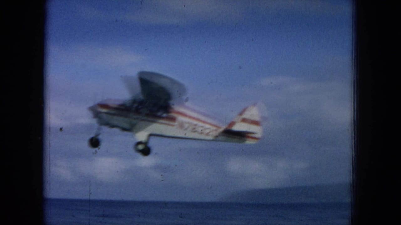 Closer view of a small propeller plane over water with registration markings visible.