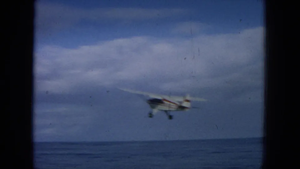 1964 Hawaii 8mm frame showing the small aircraft receding or approaching at low altitude over open water.