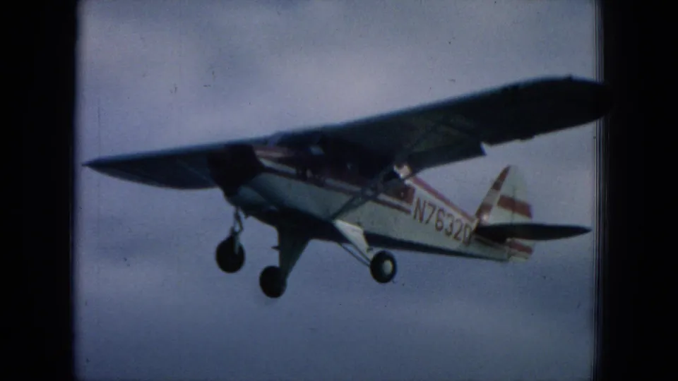 1964 Hawaii 8mm frame showing a close side view of a small single-engine plane with registration markings over water.