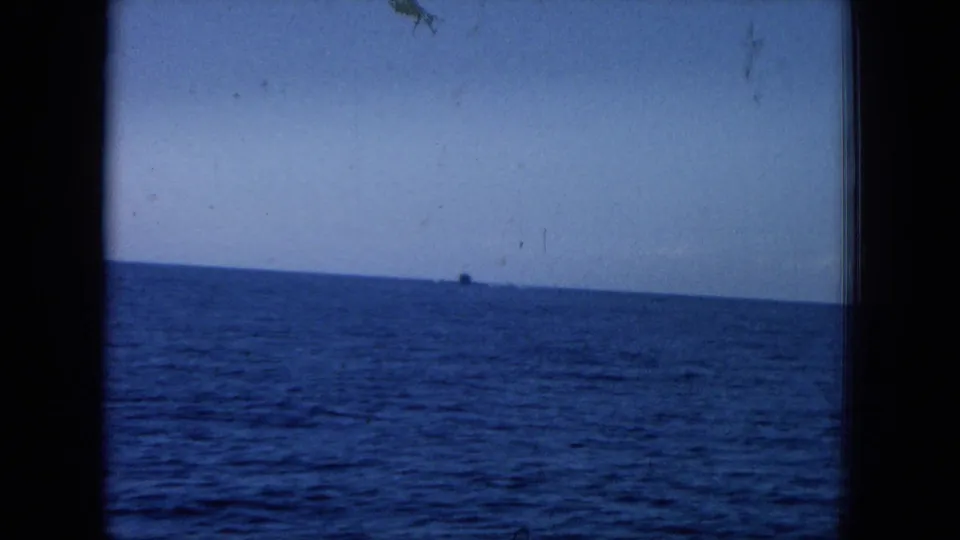 1964 Hawaii home-movie frame showing open ocean and a low horizon beneath blue sky, with a tiny dark distant shape near the horizon.