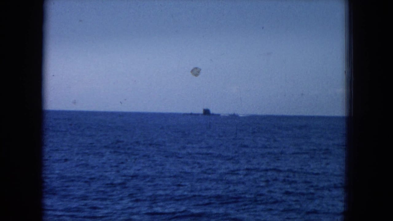 Blue ocean horizon with a small distant structure or vessel framed by dark vertical bars.