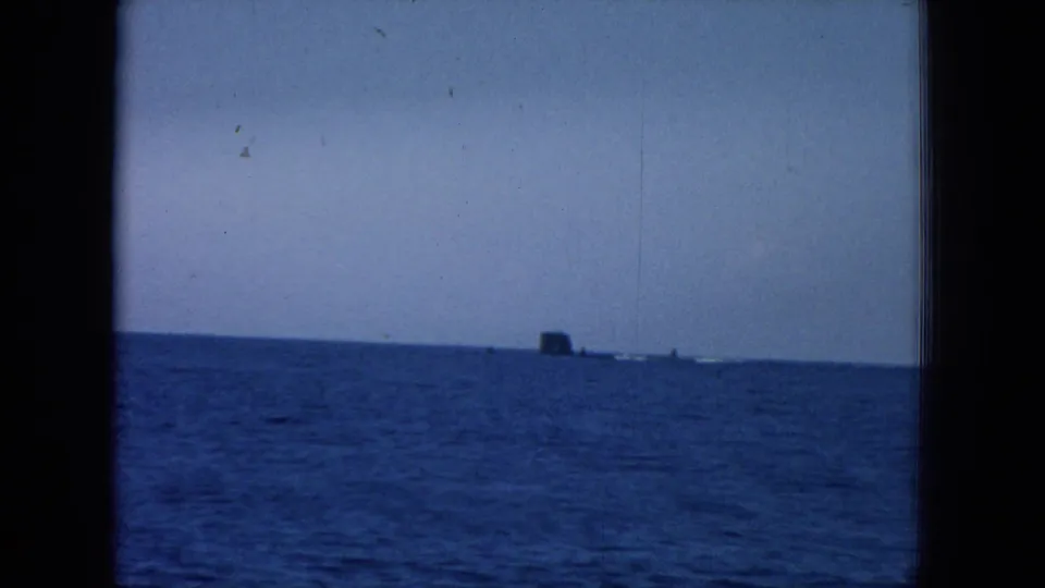 1964 Hawaii 8mm frame of the open ocean with a small dark unidentified object and faint distant shapes along the horizon.