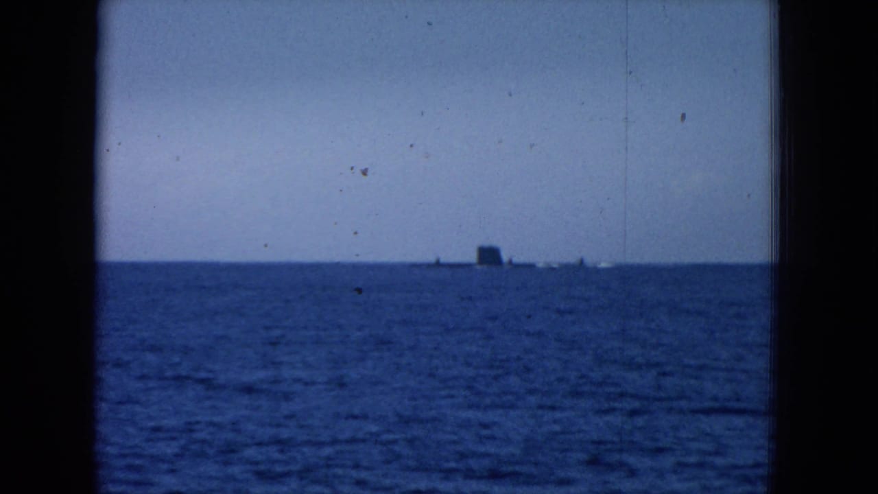 Blue-tinted 8mm frame of open water near Oahi, Hawaii, with a small distant vessel shape on the horizon.