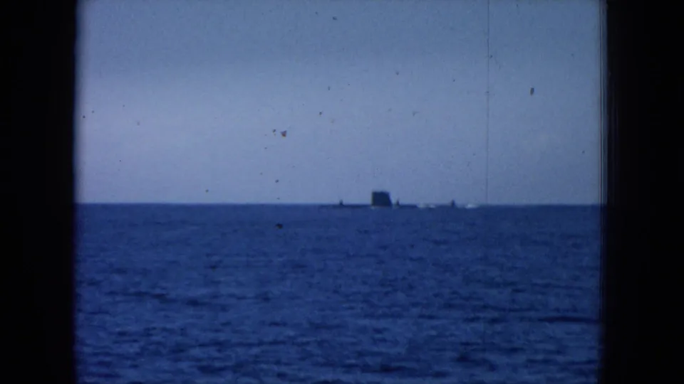 Blue-tinted 8mm frame of open water near Oahi, Hawaii, with a small distant vessel shape on the horizon.