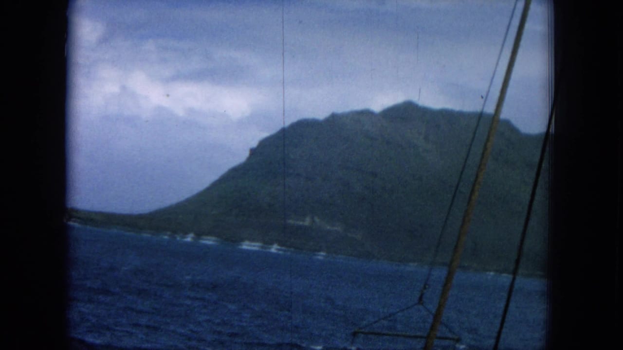Ocean view from a boat with dark coastal hills, cloudy sky, and rigging at the right edge.