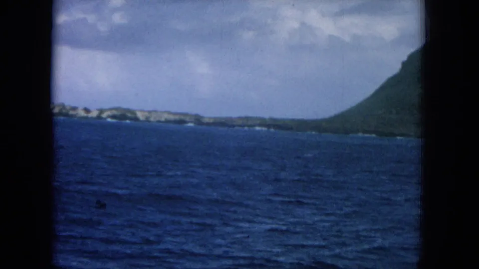 1964 Hawaii 8mm frame with open ocean, low shoreline, and a coastal hillside at the edge of the shot.
