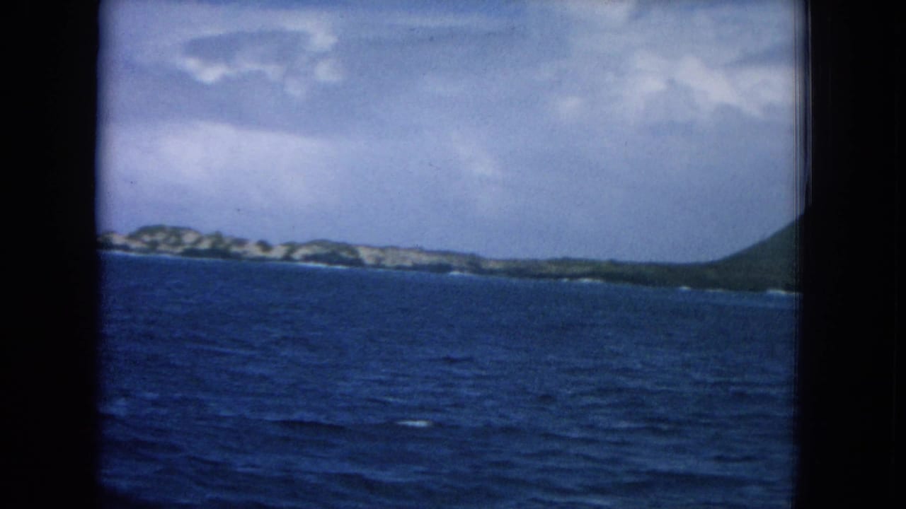 Blue ocean seen through a ship window with a distant island shoreline and cloudy sky.