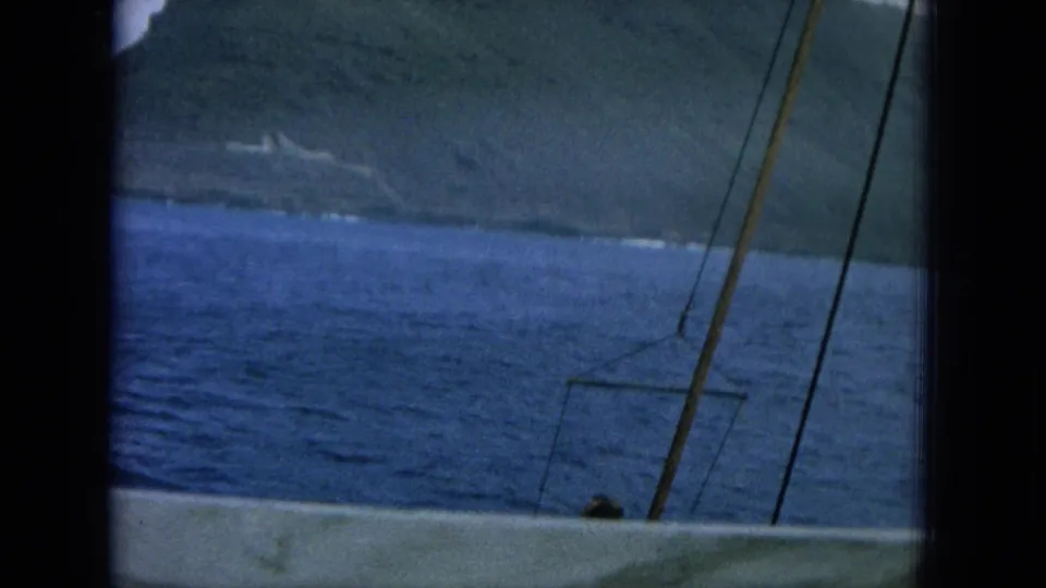A tilted 1964 Hawaii shipboard view shows ocean, nearby land or shoreline, deck edge, and mast-like lines in front.