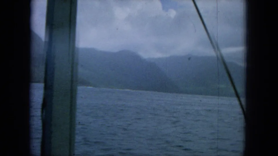 1964 8mm Hawaii frame with sailboat mast and rigging in front of hazy mountains and ocean.