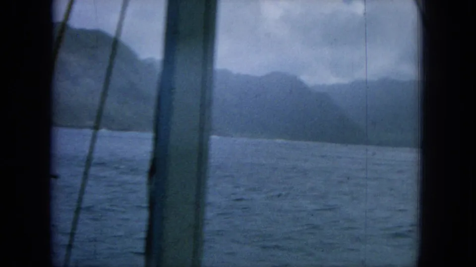 1964 8mm Hawaii boat view showing blue water, distant mountains, overcast sky, and dark vertical framing from the vessel.
