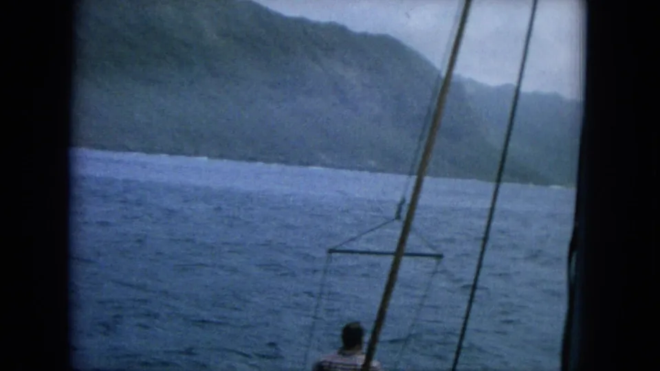 A tilted 1964 Hawaii boat view shows rigging, open water, green mountains, and a man partly visible near the lower edge.