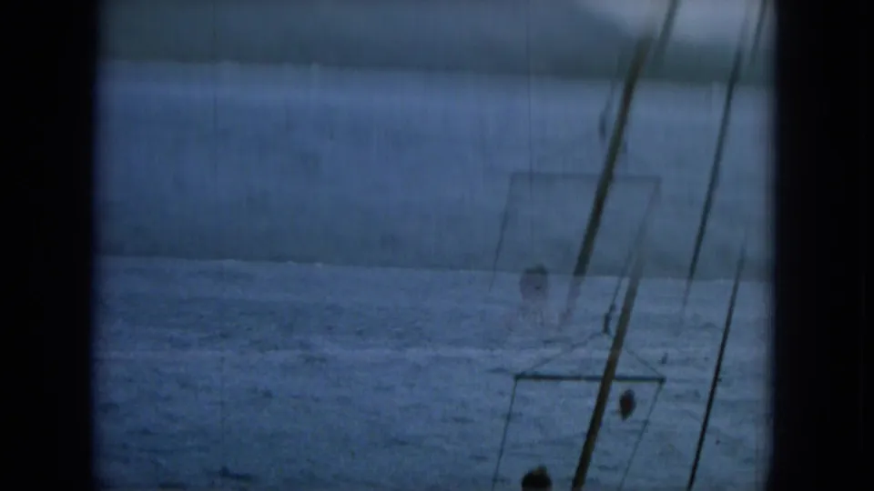Motion-soft 1964 Hawaii home-movie frame looking through a boat window at blue water, rigging, and a small passenger figure below.